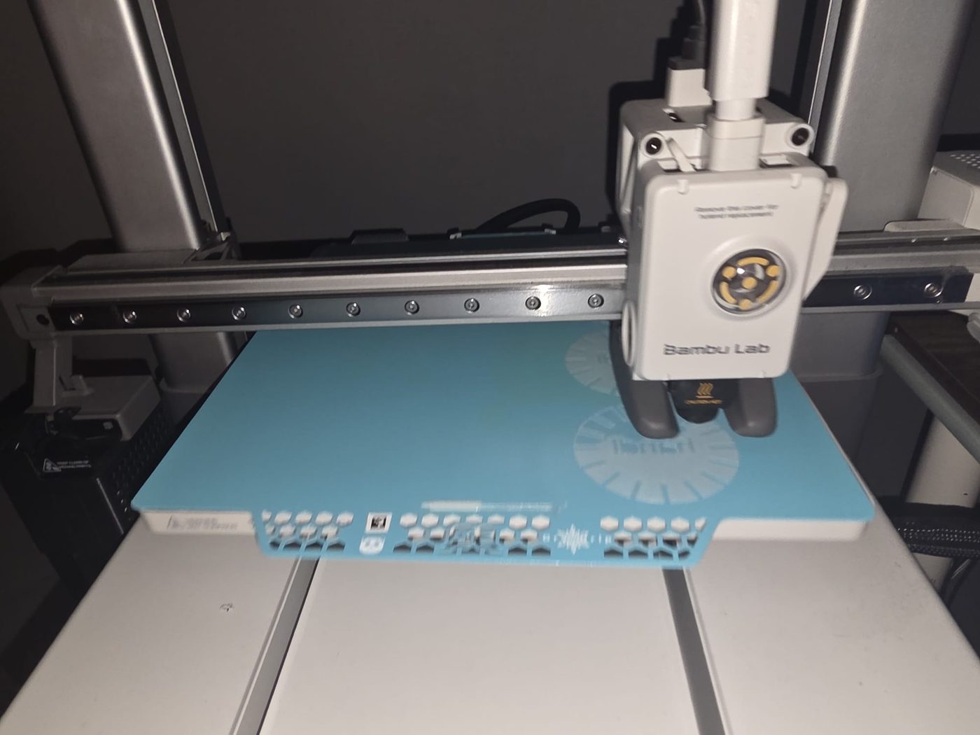 A Bambu Lab printer part-way through a job, the print head over a part on the blue bed